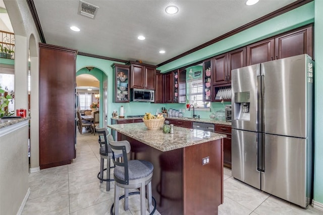 kitchen with visible vents, arched walkways, appliances with stainless steel finishes, light tile patterned flooring, and light stone countertops