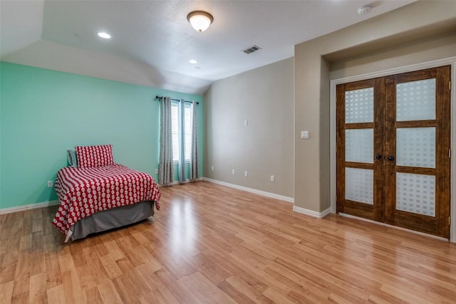 bedroom featuring light wood finished floors, visible vents, baseboards, vaulted ceiling, and french doors