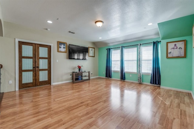 unfurnished living room with lofted ceiling, french doors, light wood-type flooring, and visible vents