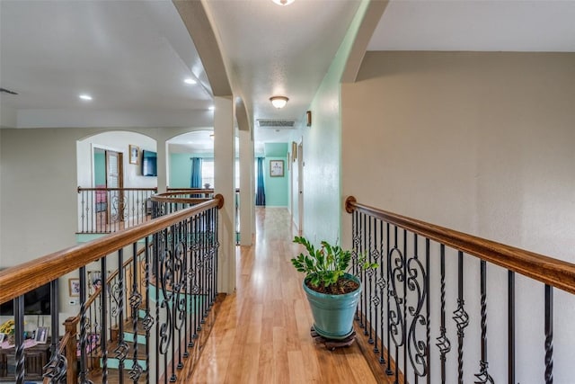 corridor with an upstairs landing, wood finished floors, and visible vents