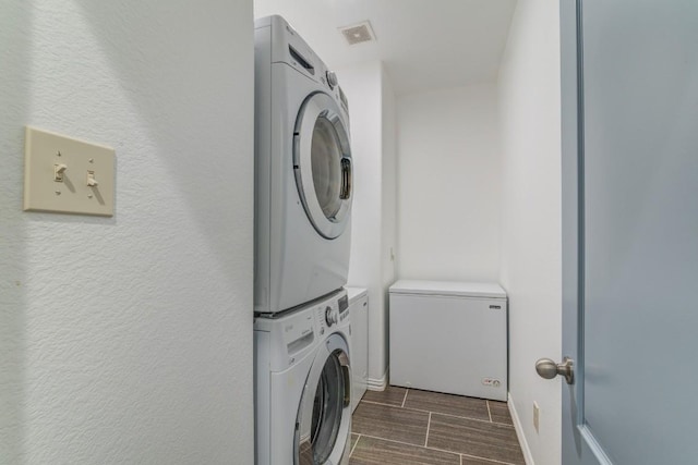 washroom with visible vents, stacked washer and dryer, laundry area, baseboards, and wood tiled floor