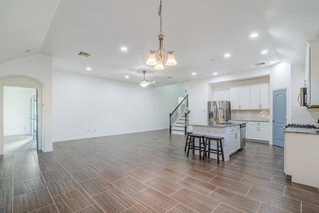 kitchen with open floor plan, decorative backsplash, stainless steel appliances, white cabinetry, and a sink