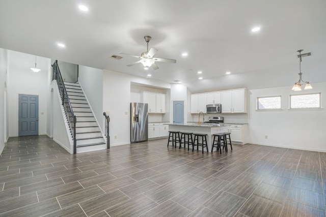 kitchen featuring a center island with sink, a breakfast bar, a sink, appliances with stainless steel finishes, and white cabinetry