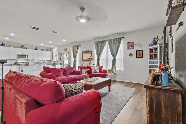 living area featuring visible vents, baseboards, light wood-style floors, and ceiling fan