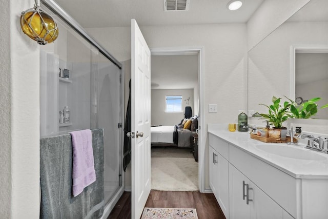 ensuite bathroom featuring visible vents, a shower stall, double vanity, wood finished floors, and a sink