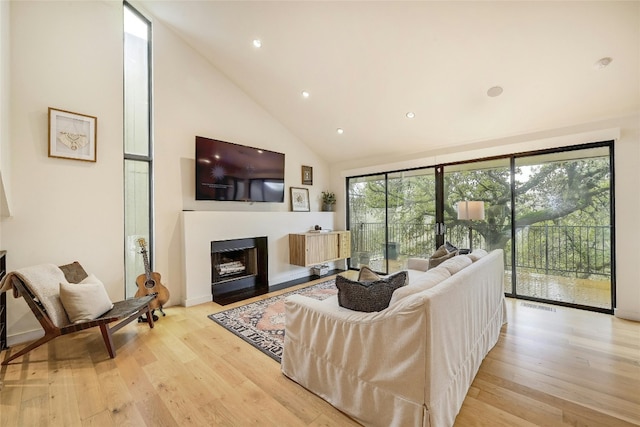 living area featuring recessed lighting, a fireplace with flush hearth, high vaulted ceiling, and light wood-style flooring