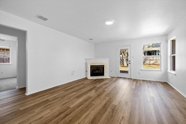 unfurnished living room featuring wood finished floors, a fireplace with raised hearth, visible vents, and a textured ceiling