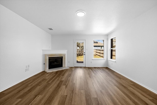 unfurnished living room with baseboards, wood finished floors, visible vents, and a fireplace with raised hearth