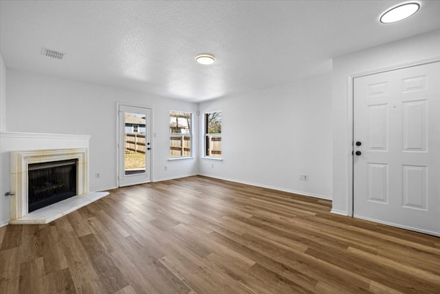 unfurnished living room with visible vents, a fireplace with raised hearth, baseboards, wood finished floors, and a textured ceiling