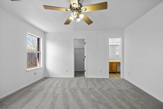 unfurnished bedroom featuring ensuite bathroom, a ceiling fan, a closet, carpet flooring, and a spacious closet