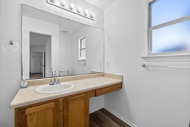 bathroom featuring visible vents, baseboards, toilet, wood finished floors, and vanity