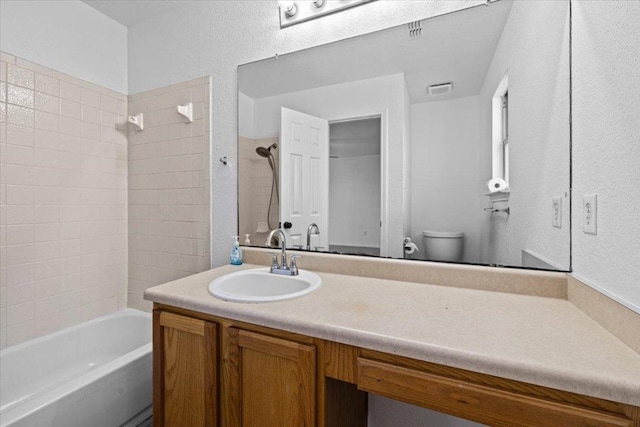 full bathroom with visible vents, toilet, shower / bathing tub combination, vanity, and a textured wall