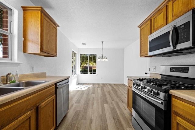 kitchen with brown cabinetry, a sink, stainless steel appliances, a notable chandelier, and light wood-type flooring