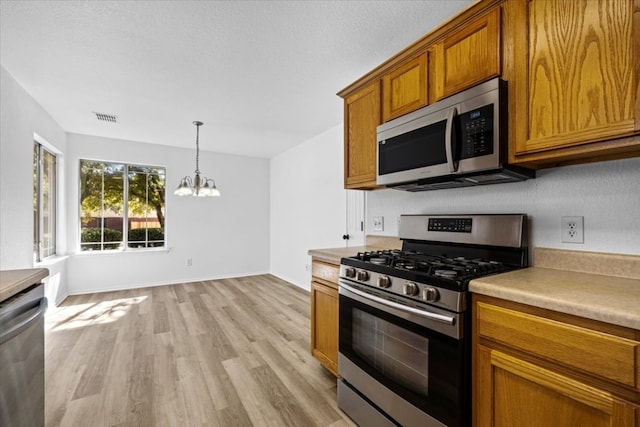 kitchen with stainless steel appliances, brown cabinets, visible vents, and an inviting chandelier