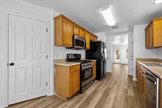 kitchen with light wood-type flooring, visible vents, brown cabinets, a sink, and stainless steel appliances