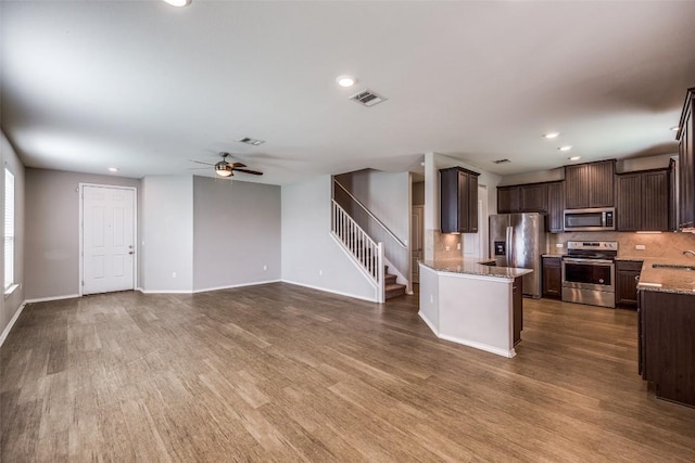 kitchen featuring dark wood-type flooring, backsplash, dark brown cabinetry, appliances with stainless steel finishes, and light stone countertops