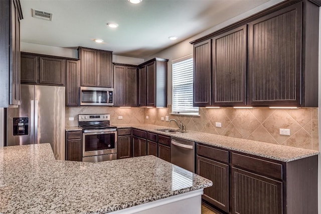 kitchen with tasteful backsplash, visible vents, dark brown cabinets, stainless steel appliances, and a sink