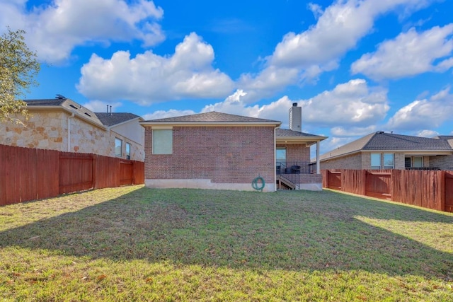 back of house featuring brick siding, a lawn, a chimney, and a fenced backyard