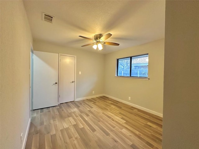 empty room featuring ceiling fan, light wood-style floors, visible vents, and baseboards