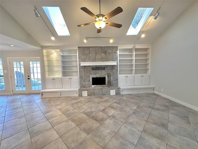 unfurnished living room featuring tile patterned flooring, baseboards, a tiled fireplace, built in features, and vaulted ceiling with skylight