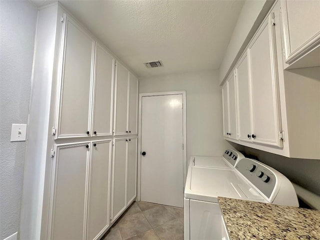 laundry area featuring visible vents, a textured ceiling, cabinet space, light tile patterned flooring, and washing machine and clothes dryer