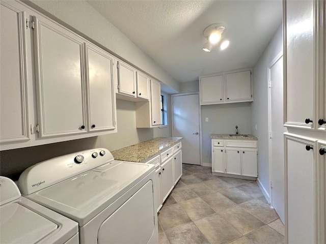 clothes washing area with a sink, baseboards, cabinet space, and washing machine and dryer