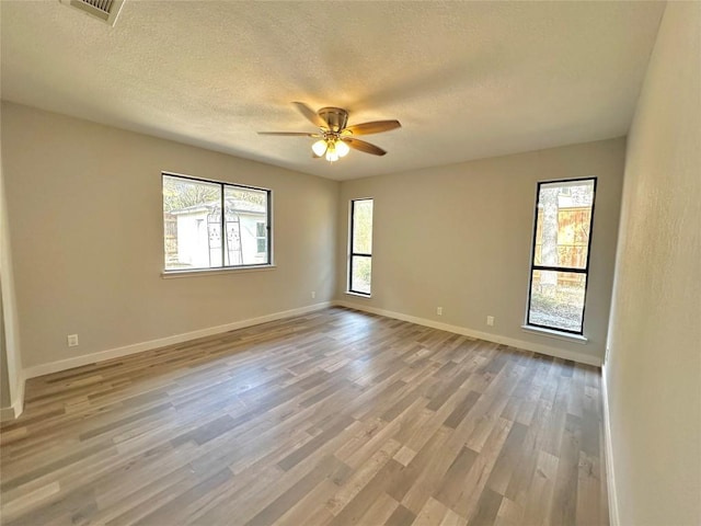 empty room with a ceiling fan, visible vents, baseboards, light wood-style flooring, and a textured ceiling