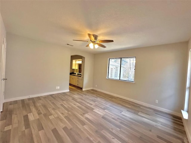 spare room featuring a ceiling fan, baseboards, light wood-style flooring, arched walkways, and a textured ceiling