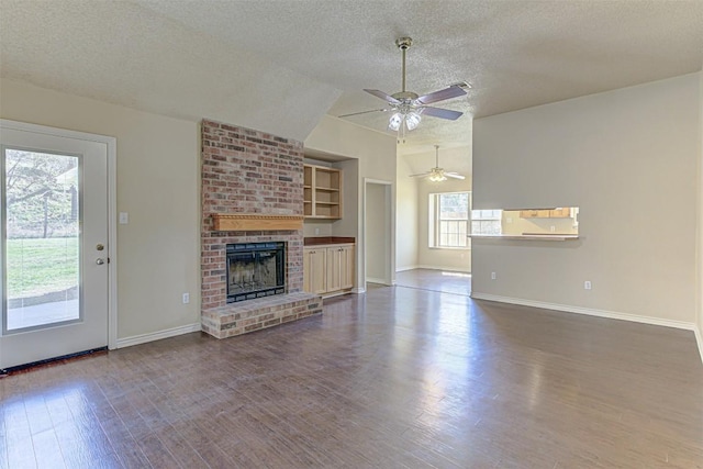 unfurnished living room with a wealth of natural light, lofted ceiling, a brick fireplace, and wood finished floors