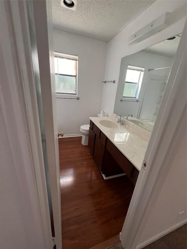 bathroom featuring baseboards, toilet, vanity, wood finished floors, and a textured ceiling