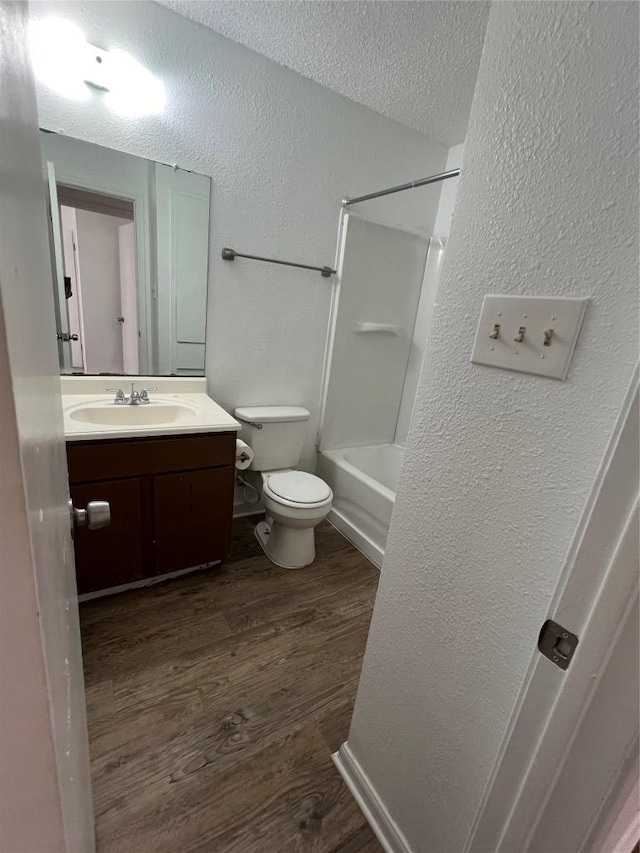 full bath featuring toilet, a textured ceiling, wood finished floors, vanity, and a textured wall