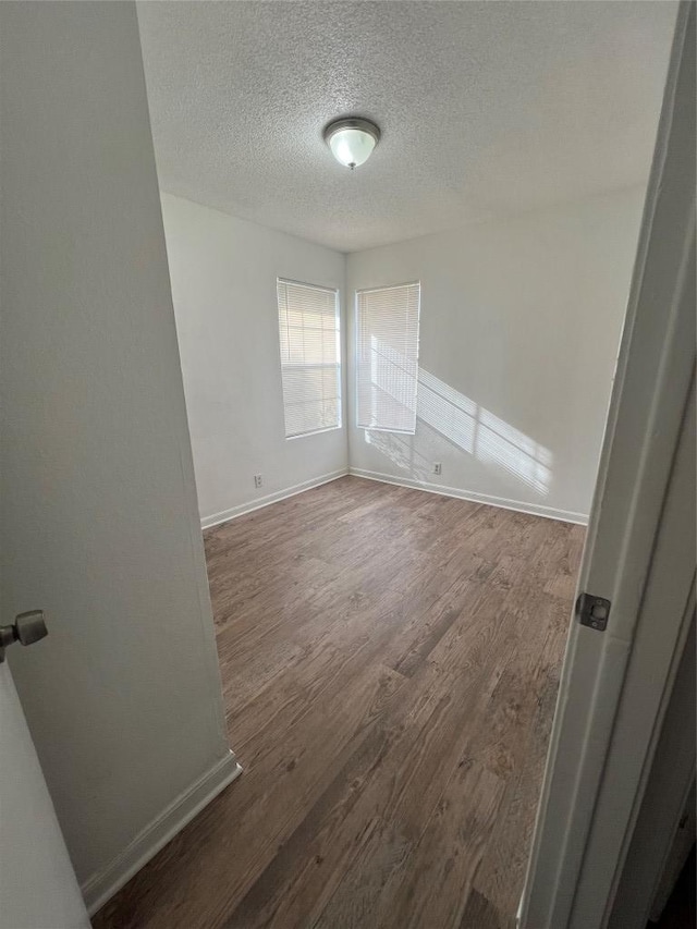 unfurnished room with baseboards, a textured ceiling, and wood finished floors