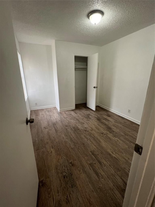 unfurnished bedroom featuring wood finished floors, baseboards, a closet, and a textured ceiling