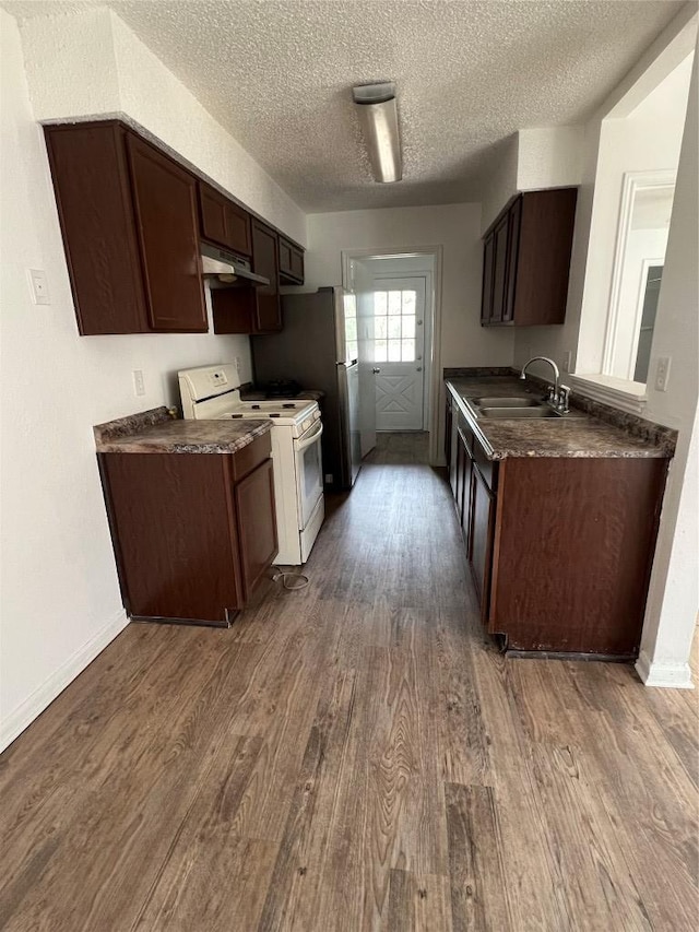 kitchen with wood finished floors, a sink, under cabinet range hood, white range, and dark countertops