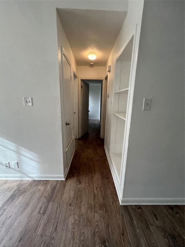 hall featuring built in features, baseboards, dark wood-type flooring, and a textured ceiling