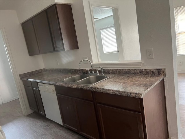 kitchen featuring a sink, dark countertops, dark brown cabinetry, white dishwasher, and light wood finished floors