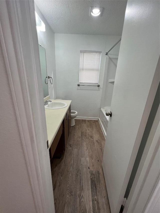 full bath featuring vanity, washtub / shower combination, wood finished floors, a textured ceiling, and toilet