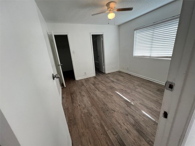 unfurnished bedroom featuring a spacious closet, a textured ceiling, baseboards, and wood finished floors