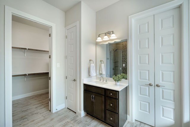 bathroom with vanity, wood finished floors, baseboards, a stall shower, and a walk in closet