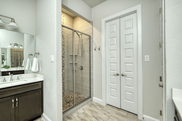 bathroom with vanity, wood finished floors, baseboards, a shower stall, and a closet