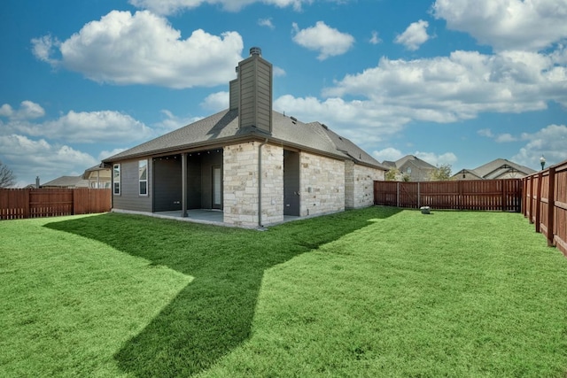 rear view of house with a yard, a fenced backyard, a chimney, and a patio area