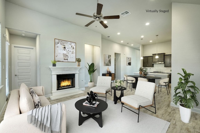 living area featuring baseboards, visible vents, light wood finished floors, recessed lighting, and a lit fireplace