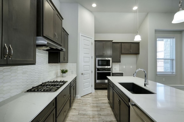 kitchen featuring a sink, decorative backsplash, stainless steel appliances, under cabinet range hood, and pendant lighting