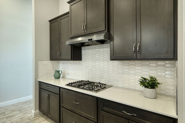 kitchen with under cabinet range hood, tasteful backsplash, light countertops, and stainless steel gas stovetop