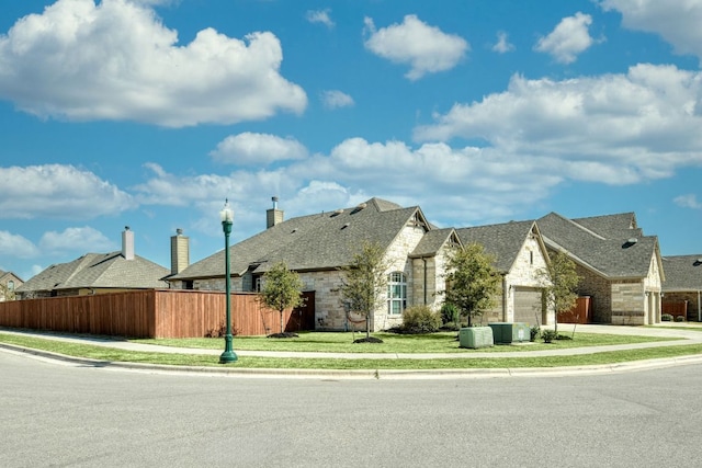 view of front of home featuring an attached garage, fence, stone siding, and driveway