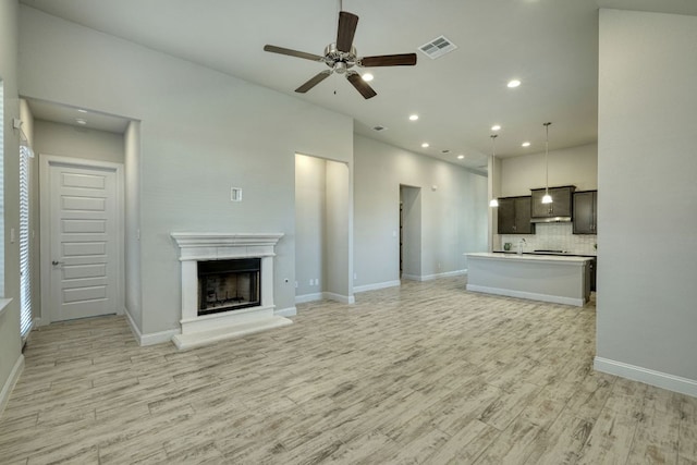 unfurnished living room with visible vents, a fireplace with raised hearth, recessed lighting, light wood-style floors, and baseboards