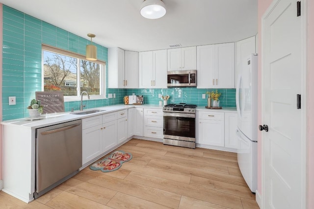 kitchen featuring a sink, decorative backsplash, light countertops, stainless steel appliances, and light wood-type flooring