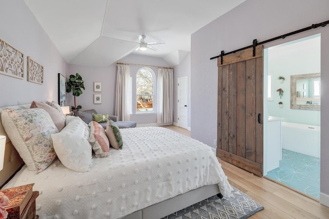 bedroom featuring light wood finished floors, ceiling fan, a barn door, vaulted ceiling, and ensuite bath