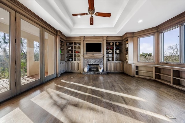 unfurnished living room with a tray ceiling, plenty of natural light, dark wood-style floors, and a fireplace