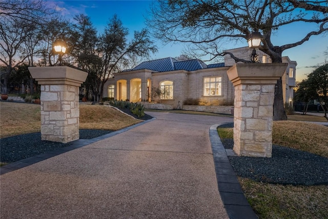 view of front of property featuring metal roof, stone siding, driveway, and a standing seam roof